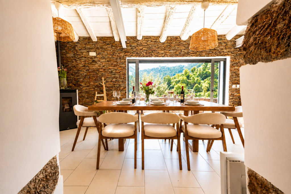 Rustic dining room with exposed wooden beams, natural stone walls and open doors overlooking the mountains at Peregrinus Rio de Frades country house in Arouca, Portugal.