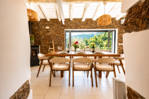 Rustic dining room with exposed wooden beams, natural stone walls and open doors overlooking the mountains at Peregrinus Rio de Frades country house in Arouca, Portugal.